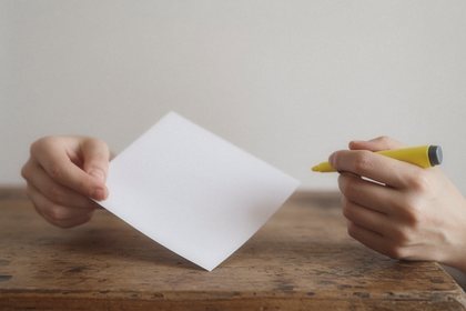 Hands hold a blank page and a yellow highlighter over a wooden desk